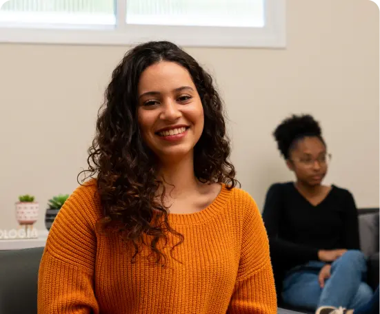 Moça sorrindo para a camera, com a blusa de cor alaranjada